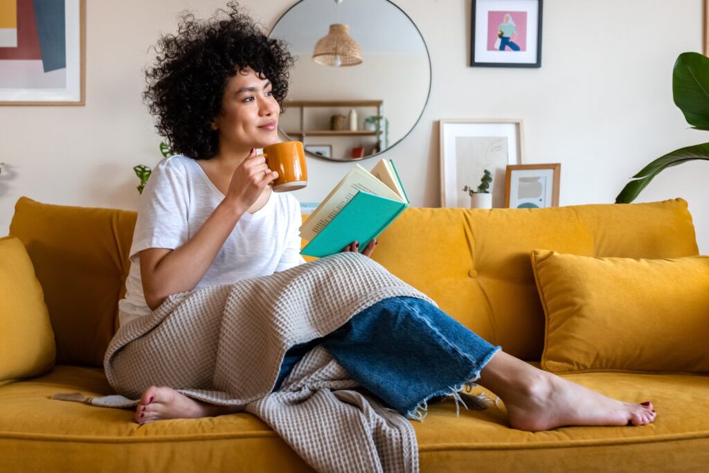 Common Furnace Issues That a Tune-Up Can Prevent 1 A person on a couch in a blanket, with a mug in one hand and a book in the other.