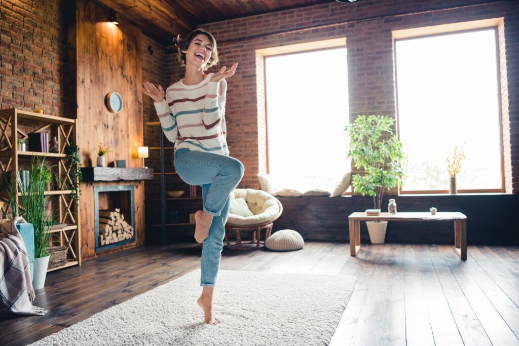 Best Rooms to Install Radiant Heating in For Maximum Comfort 1 A happy person dancing on a rug in the middle of a modern, exposed-brick living room.