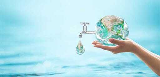 Hand holding water faucet shaped like Earth with droplet.