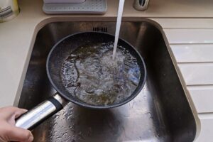 A greasy pan getting washed in a sink